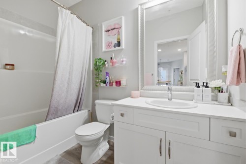 The bathroom features a bathtub with a shower, a toilet, and a vanity with a sink and storage - 155 1818 Rutherford Road, Edmonton, AB - Indoor Photo Showing Bathroom