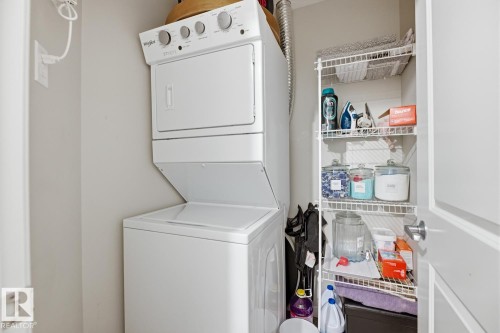 Laundry area featuring a stacked washer and dryer unit, and an adjacent storage shelf - 155 1818 Rutherford Road, Edmonton, AB - Indoor Photo Showing Laundry Room