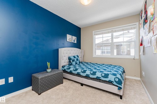 This room features a window providing natural light, a neutral-toned carpet, and a wall with a vibrant blue accent - 31 4029 Orchards Drive, Edmonton, autreother - Indoor Photo Showing Bedroom