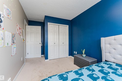 This room features soft carpet flooring, a closet with bi-fold doors, and a neutral wall color complemented by a vibrant blue accent wall - 31 4029 Orchards Drive, Edmonton, autreother - Indoor Photo Showing Bedroom