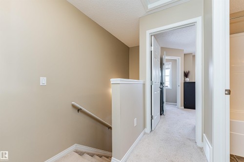 The property features carpeted stairs with a white handrail, leading to a carpeted hallway with a doorway to an additional room - 31 4029 Orchards Drive, Edmonton, autreother - Indoor Photo Showing Other Room