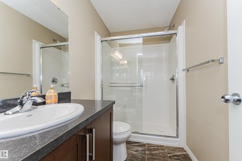Bathroom featuring a vanity with a white oval sink and dark countertop, a walk-in shower with a glass enclosure, and dark tiled flooring - 31 4029 Orchards Drive, Edmonton, autreother - Indoor Photo Showing Bathroom