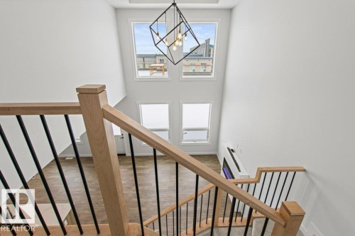 This property features a contemporary chandelier, large windows providing natural light, and a staircase with light-toned wood banisters and black balusters - 5018 53 Avenue, Calmar, AB - Indoor Photo Showing Other Room