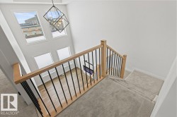 This interior view features a staircase with light wood railings and black vertical balusters, leading down to a carpeted landing - 