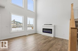 Living space featuring high ceilings, large windows, an electric fireplace, and light wood flooring - 