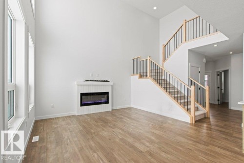 Living area featuring high ceilings, light-toned flooring, a fireplace, and large windows - 5018 53 Avenue, Calmar, AB - Indoor With Fireplace