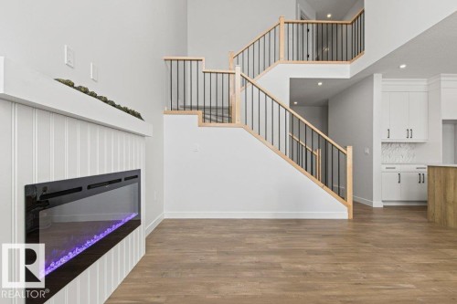 The property features an electric fireplace with a white shiplap surround, hardwood floors, and a staircase with light wood handrails and black balusters - 5018 53 Avenue, Calmar, AB - Indoor Photo Showing Other Room