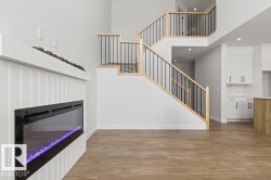 The property features an electric fireplace with a white shiplap surround, hardwood floors, and a staircase with light wood handrails and black balusters - 