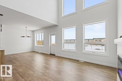 This open-concept living area features high ceilings, light wood-look flooring, and several large windows that provide abundant natural light - 