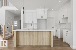 The kitchen features white cabinetry with black hardware, a light-toned wood island with a white countertop, and a white marble-patterned backsplash - 
