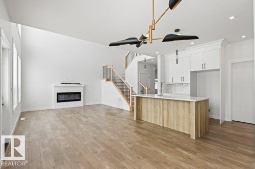 This open-concept living area features light wood-style flooring, a contemporary fireplace, and a kitchen island with a light-colored countertop - 5018 53 Avenue, Calmar, AB - Indoor Photo Showing Kitchen