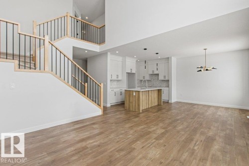 Open-concept living space featuring light-toned flooring, a two-story staircase with light wood and black metal railings, and a kitchen with white cabinetry and an island - 5018 53 Avenue, Calmar, AB - Indoor
