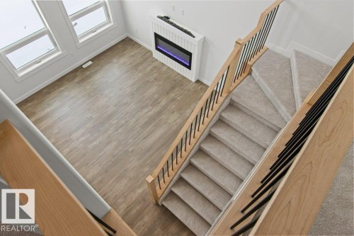 The property features a staircase with light wood banisters and black spindles, leading to a living area with light wood-style flooring - 5018 53 Avenue, Calmar, AB - Indoor Photo Showing Other Room