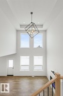 Spacious living area featuring high ceilings, large windows providing natural light, a modern light fixture, and hardwood flooring - 