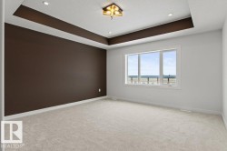 Spacious room featuring light-colored carpet, a large window, and a tray ceiling with recessed lighting and a central light fixture - 