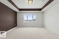 Spacious room featuring light-colored carpeting, a large window, and a tray ceiling with recessed lighting and a central light fixture - 