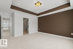 Spacious room featuring light-colored carpeting, a brown accent wall, and a tray ceiling with recessed lighting and a decorative light fixture - 
