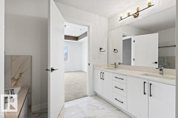 The bathroom features a double vanity with white cabinetry, light-colored countertops, and modern dark hardware - 
