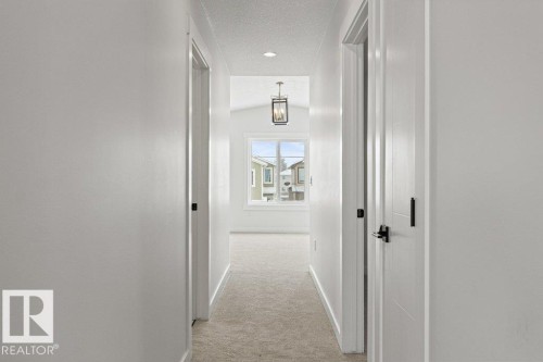 Hallway with light-colored walls and carpeting, featuring several doors with dark hardware, and a window providing natural light at the far end - 5018 53 Avenue, Calmar, AB - Indoor Photo Showing Other Room