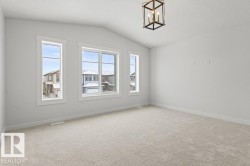 This room features light-colored carpet flooring, white walls, and a vaulted ceiling with a decorative light fixture - 