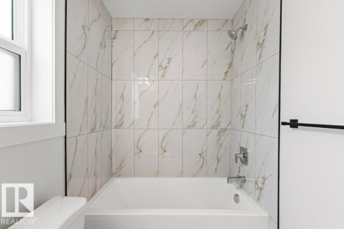 The bathroom features a bathtub with a shower, surrounded by large format marble-look tiles - 5018 53 Avenue, Calmar, AB - Indoor Photo Showing Bathroom