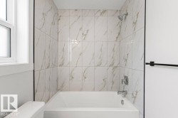 The bathroom features a bathtub with a shower, surrounded by large format marble-look tiles - 