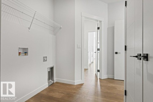 Laundry area with hardwood flooring, a white wire shelf, and modern white doors with black hardware - 5018 53 Avenue, Calmar, AB - Indoor