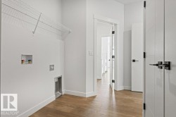 Laundry area with hardwood flooring, a white wire shelf, and modern white doors with black hardware - 