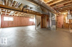 Spacious unfinished basement offering an expansive concrete floor, visible wooden joists, and two windows providing natural light - 