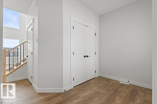 This area features warm-toned flooring, white walls, and a staircase with a wooden handrail and black metal balusters - 5018 53 Avenue, Calmar, AB - Indoor Photo Showing Other Room