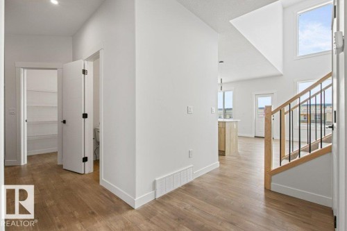 Open concept living area featuring hardwood flooring, an open staircase with a wooden handrail and black balusters, and large windows providing ample natural light - 5018 53 Avenue, Calmar, AB - Indoor Photo Showing Other Room