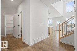 Open concept living area featuring hardwood flooring, an open staircase with a wooden handrail and black balusters, and large windows providing ample natural light - 
