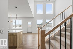 This open-concept interior features high ceilings, light wood flooring, and a modern staircase with carpeted treads and wooden handrails - 
