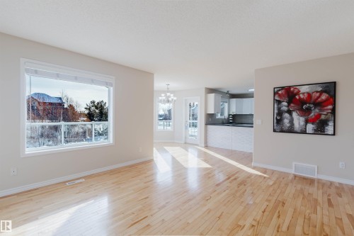 Bright and airy interior featuring light hardwood flooring throughout, a large window providing views of the outdoors, and a well-appointed kitchen with white cabinetry - 1135 112 Street, Edmonton, AB - Indoor Photo Showing Living Room