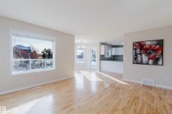 Bright and airy interior featuring light hardwood flooring throughout, a large window providing views of the outdoors, and a well-appointed kitchen with white cabinetry - 