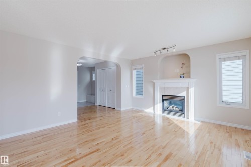 This living space features hardwood floors, a gas fireplace with a mantel, and two windows with blinds - 1135 112 Street, Edmonton, AB - Indoor Photo Showing Living Room With Fireplace