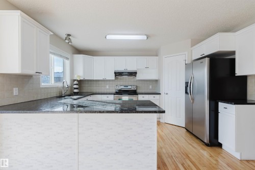The kitchen features white cabinetry, dark countertops, hardwood flooring, and stainless steel appliances, including a side-by-side refrigerator and a range - 1135 112 Street, Edmonton, AB - Indoor Photo Showing Kitchen