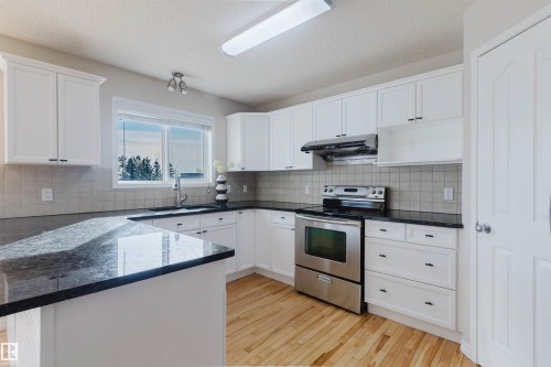 The kitchen features white cabinetry, dark countertops, a light-colored tile backsplash, stainless steel appliances, and wood flooring - 1135 112 Street, Edmonton, AB - Indoor Photo Showing Kitchen