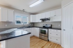 The kitchen features white cabinetry, dark countertops, a light-colored tile backsplash, stainless steel appliances, and wood flooring - 