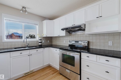 This kitchen features white cabinetry, dark countertops, and a tiled backsplash - 1135 112 Street, Edmonton, AB - Indoor Photo Showing Kitchen With Double Sink