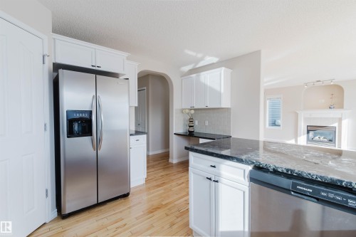 The kitchen features a stainless steel side-by-side refrigerator, white cabinetry, a dishwasher, and dark stone countertops - 1135 112 Street, Edmonton, AB - Indoor Photo Showing Kitchen With Upgraded Kitchen