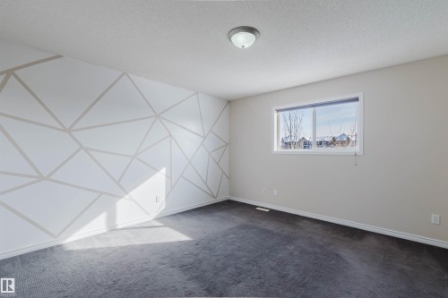 This room features a window providing natural light, dark carpeting, and a unique accent wall with a geometric pattern - 1135 112 Street, Edmonton, AB - Indoor Photo Showing Other Room