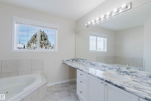 Bathroom featuring a corner bathtub with tiled surround, a vanity with a marble-patterned countertop and an integrated sink, and a large wall mirror with vanity lighting - 1135 112 Street, Edmonton, AB - Indoor Photo Showing Bathroom