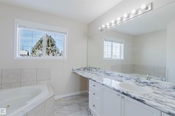 Bathroom featuring a corner bathtub with tiled surround, a vanity with a marble-patterned countertop and an integrated sink, and a large wall mirror with vanity lighting - 