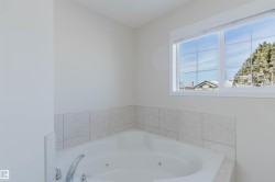 Corner bathtub featuring a tiled surround, chrome fixtures, and a window providing natural light - 