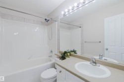 Bathroom featuring a white bathtub and shower with tiled surround, a vanity with a light-colored countertop and an integrated sink, and a large mirror with overhead lighting - 
