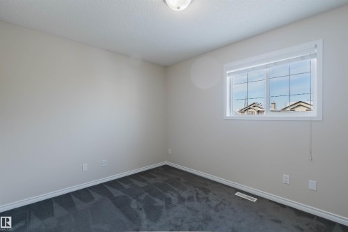 This room features neutral-toned walls, dark patterned carpeting, and a window with white trim - 1135 112 Street, Edmonton, AB - Indoor Photo Showing Other Room