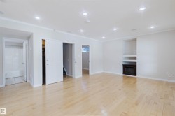 Spacious room featuring light-toned wood flooring, recessed lighting, and a built-in fireplace with shelving - 