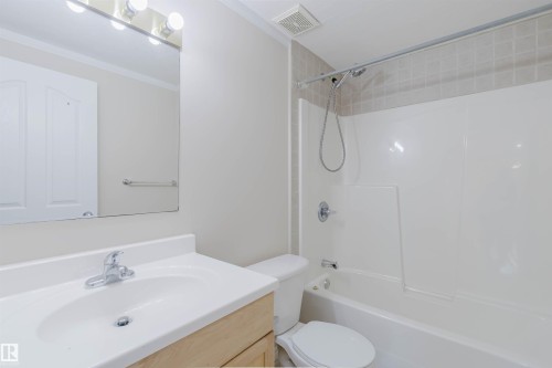 Bathroom featuring a vanity with an integrated sink and chrome faucet, a large mirror with overhead lighting, and a bathtub with a shower - 1135 112 Street, Edmonton, AB - Indoor Photo Showing Bathroom