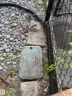 The property features a utility access panel and a black chain link fence - 